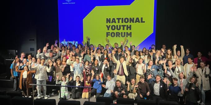 Image of large group of young people in a presentation room in front of a banner saying National Youth Forum