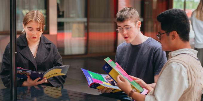 Three young people sitting around a table reading pamphlets