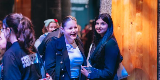 Image of two young people in a busy hallway smiling at the camera.