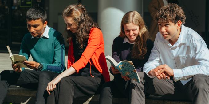 Image of four young people sitting on the steps of a building chatting.