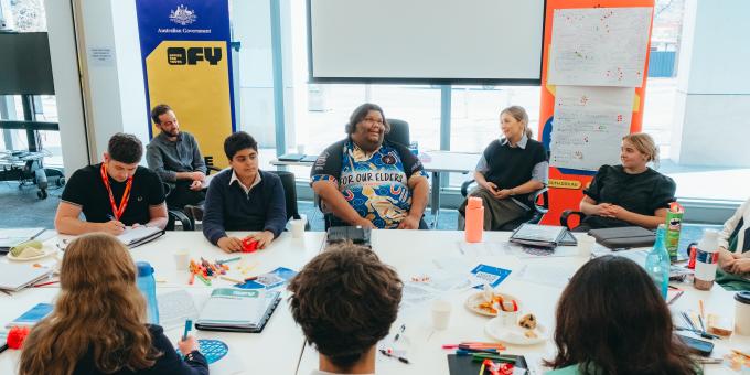 A group of young people sitting around a meeting table that is covered in notes and post its having a pleasant discussion.