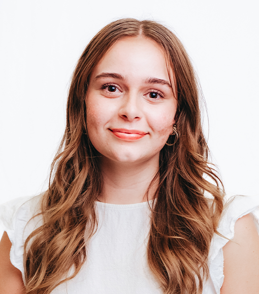 Charlotte - headshot of a smiling young woman with long brown hair wearing a white blouse.