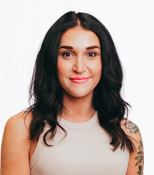 Rachel - headshot of smiling young person with shoulder length dark hair wearing a beige sleeveless top.