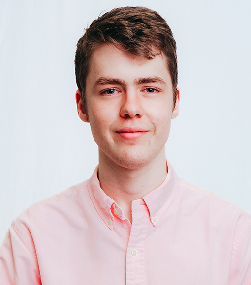 Sebastian - headshot of a young man with short brown hair wearing a pink collared shirt.