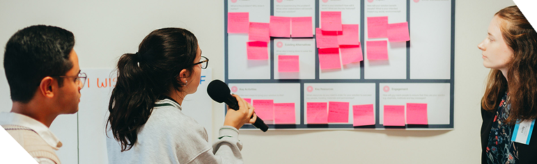 Image of three people standing in front of and reading the post-it notes on a Kanban board.