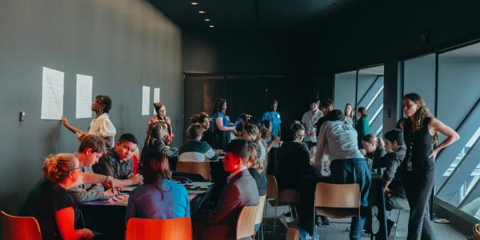 Room of people sitting at round tables having numerous discussions.