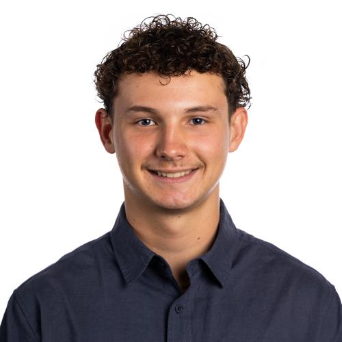 Image of Declan smiling with short curly hair and a long sleeved, collared shirt.