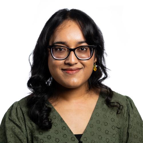 Image of Faaiza. A woman wearing glasses smiling at the camera with shoulder length hair wearing along sleeved top.