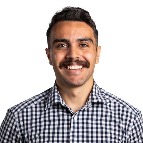 Head shot of Jeremy smiling at the camera, with short hair and a moustache, wearing a collared shirt.