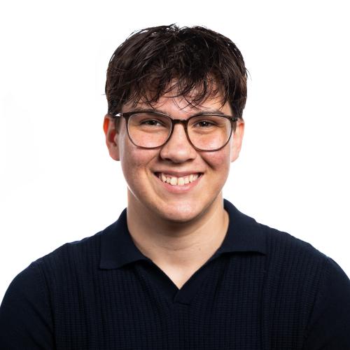 Head shot of Lucas smiling at the camera wearing spectacles and a collared tshirt.