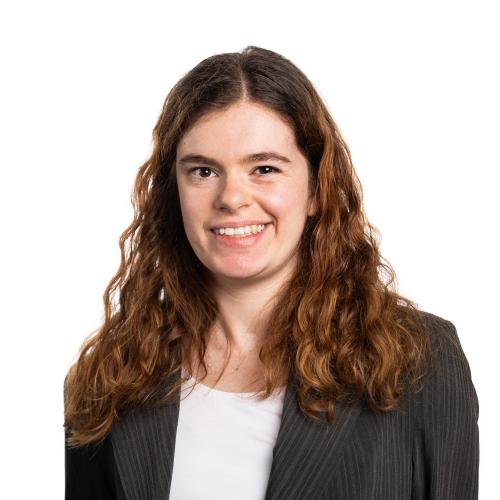 Headshot of Nicole smiling at the camera with long, wavy hair, a t-shirt and a jacket.