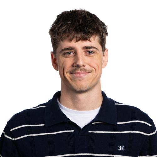 Image of Tenason smiling at the camera with short hair and a moustache.